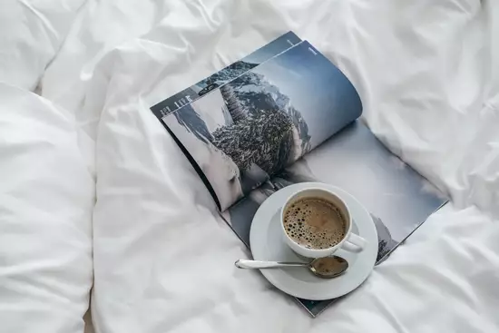 Aufgeschlagenes Magazin und Kaffeetasse auf einer Bettdecke