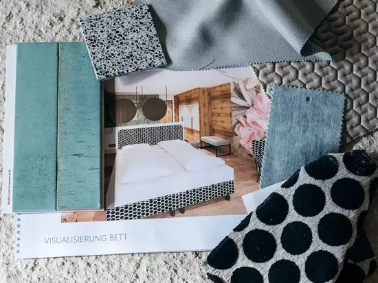 Das Bild zeigt eine Designkollektion für ein Schlafzimmer. Es umfasst Muster von Stoffen und Materialien, darunter graue und schwarze Textilien sowie einen Katalog mit einem abgebildeten Bett. Der Fokus liegt auf verschiedenen Texturen und Farben, die zur Raumgestaltung verwendet werden können.