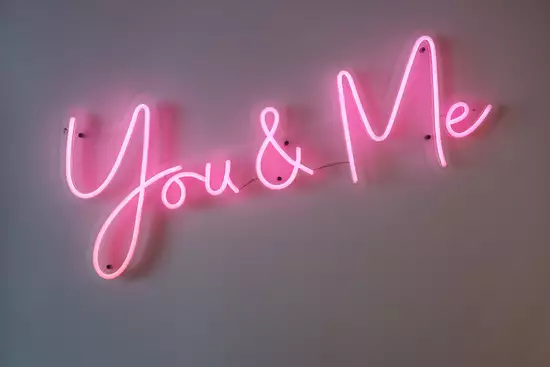 Ein neonfarbener Schriftzug auf einer Wand mit den Worten "You & Me" in pinker Farbe. Die Buchstaben sind in einer verspielten, geschwungenen Schriftart gestaltet.