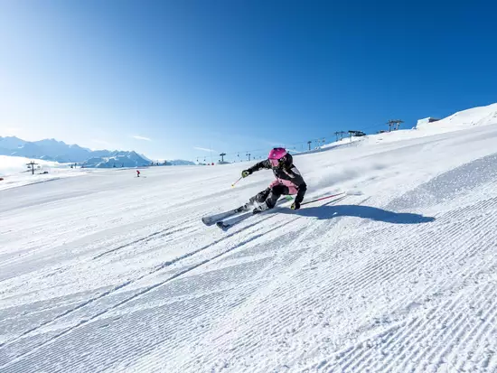Skifahrer auf leerer Piste vor blauem Himmel